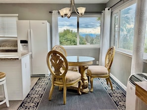 A kitchen with a refrigerator, a dining table with chairs, and a view of greenery outside.