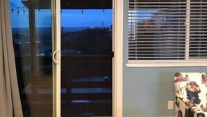 A room with a sliding glass door leading to a balcony, a window with blinds, a patterned sofa, and a wooden floor. - Great View Guest Unit/Near Eden Hospital/Kaiser SL (San Leandro)