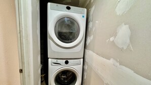 Máquina de lavar e secadora empilhadas em um cômodo com paredes sem acabamento.