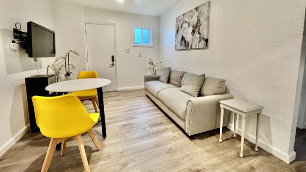 Um espaço de estar compacto com área de jantar, um sofá, uma mesa pequena e uma televisão fixada na parede.