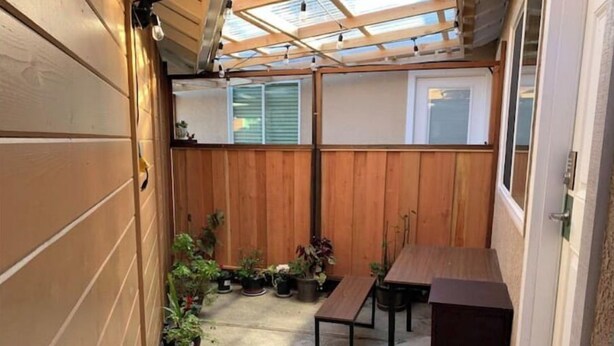 Un patio cubierto con paredes de madera, suelo de concreto y varias plantas en macetas.