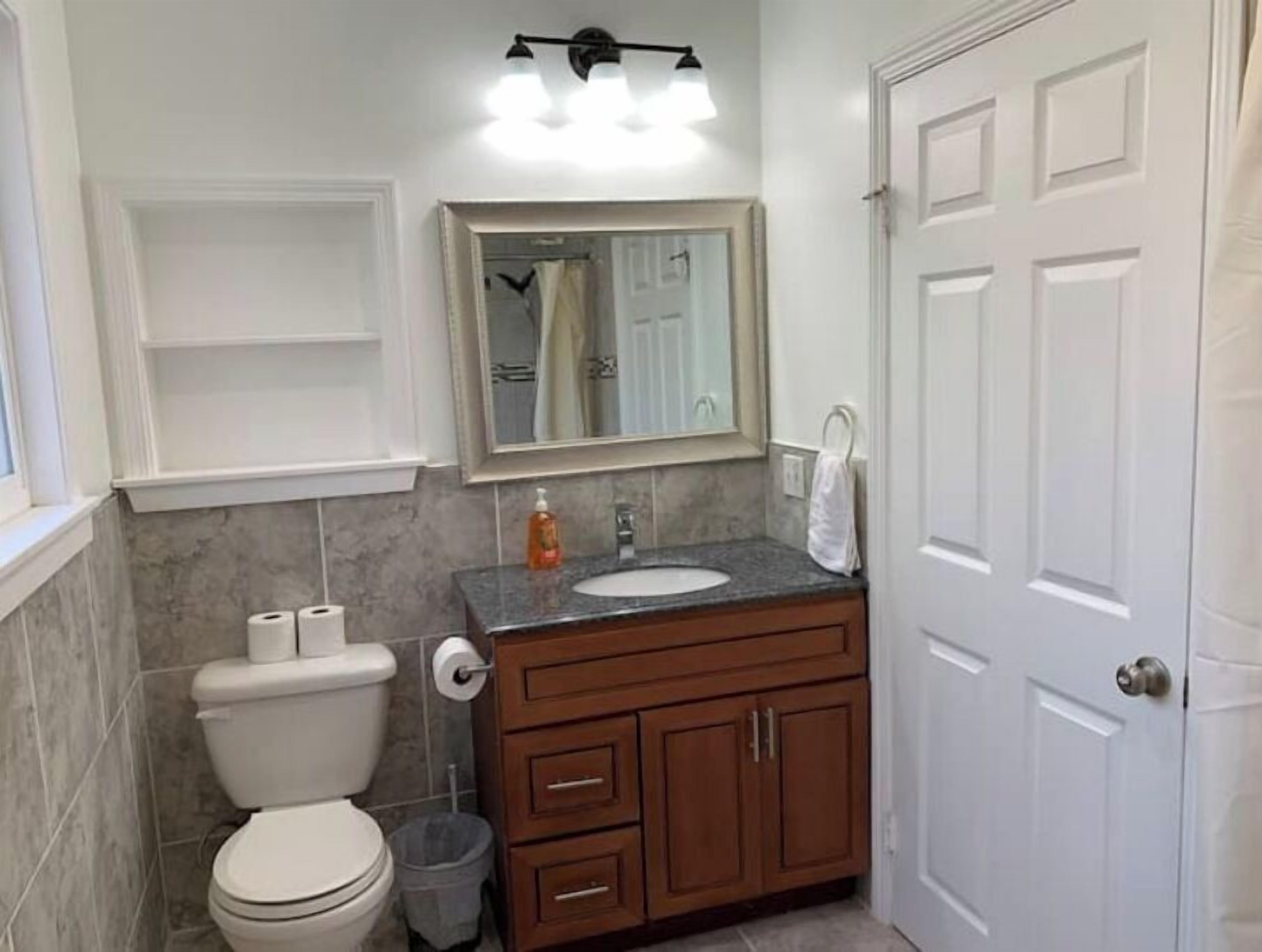 A bathroom with a toilet, sink, vanity, and a mirror.
