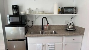 Cocina compacta con refrigerador, microondas, hervidor y pileta.