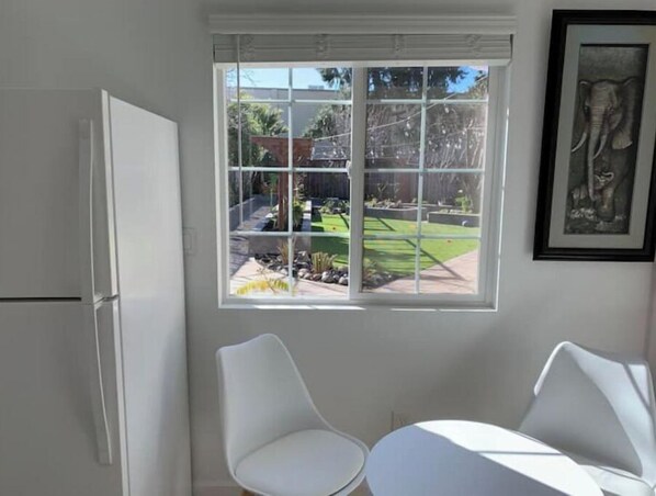 Une pièce avec une grande fenêtre, deux chaises blanches, une petite table et une porte blanche.
