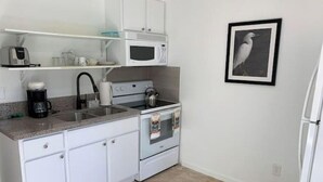 Une cuisine compacte avec des meubles blancs, un four à micro-ondes, une bouilloire et une machine à café.