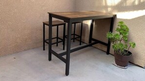 Une petite table d’angle avec un plateau en bois et un cadre en métal noir, agrémentée d’une plante en pot.