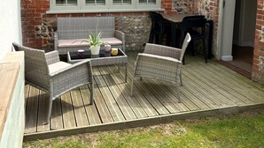 Eine Terrasse mit Korbmöbeln, einer Steinmauer und einem Backsteinhaus.