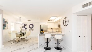 A modern kitchen with white cabinets, a marble countertop, and a clock on the wall.