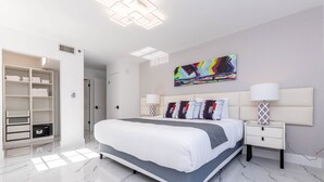A modern bedroom with a large bed, a walk-in closet, and a colorful abstract painting on the wall.