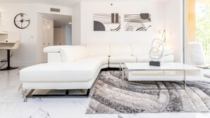 A modern living room with a white sectional sofa, a glass coffee table, abstract wall art, and a marble floor.