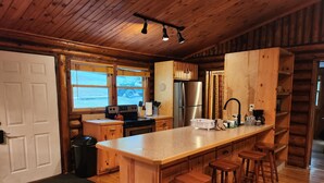 Cocina de cabaña de madera con una isla central, taburetes de bar, un refrigerador y una estufa.