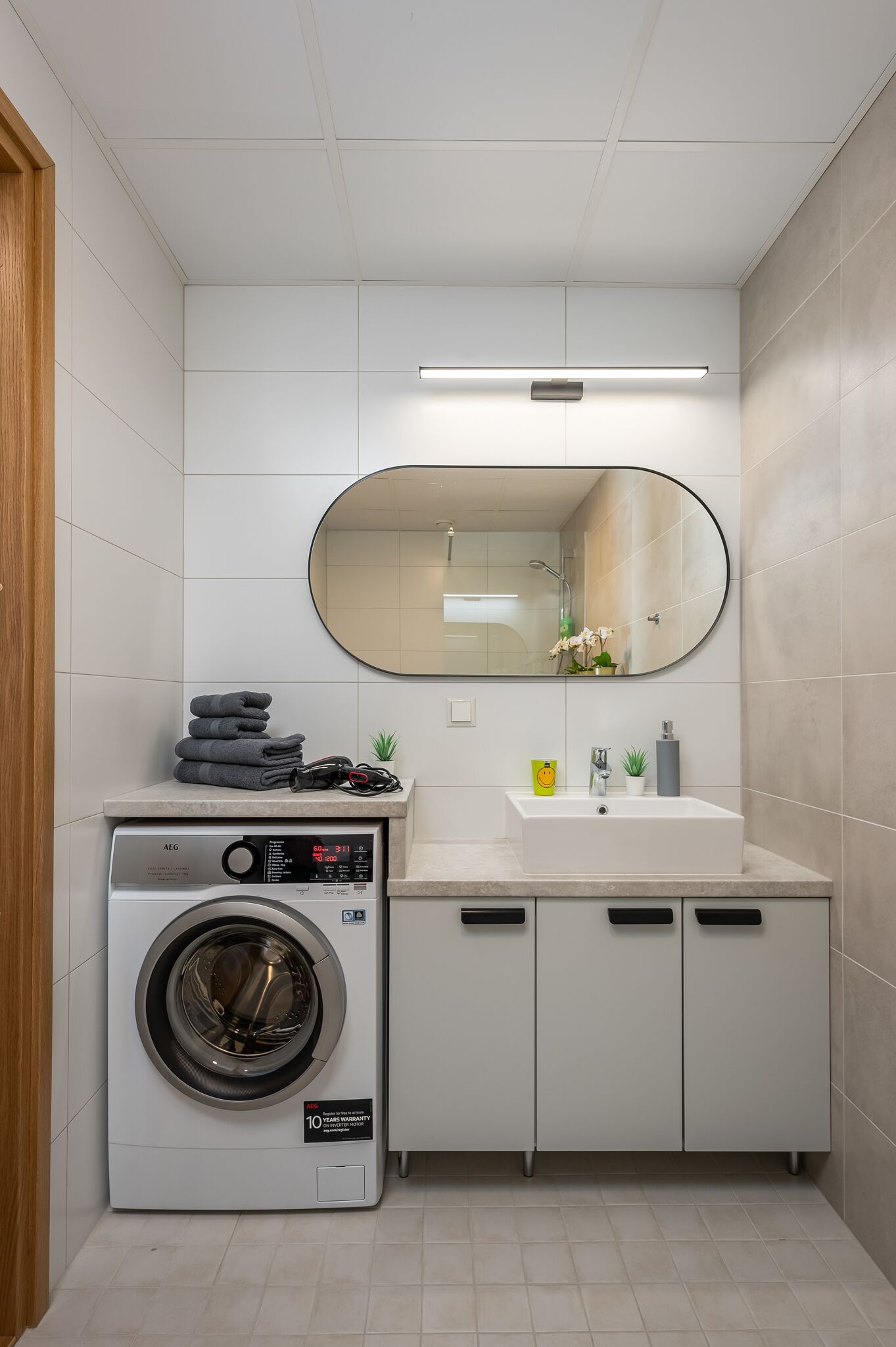 Een compacte, moderne badkamer met een ingebouwde wasmachine, een wastafel en een spiegel.