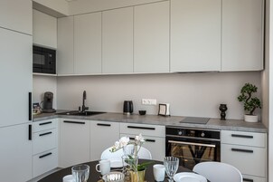 Una cocina moderna con armarios blancos, un microondas integrado y un comedor con una mesa lista para dos.