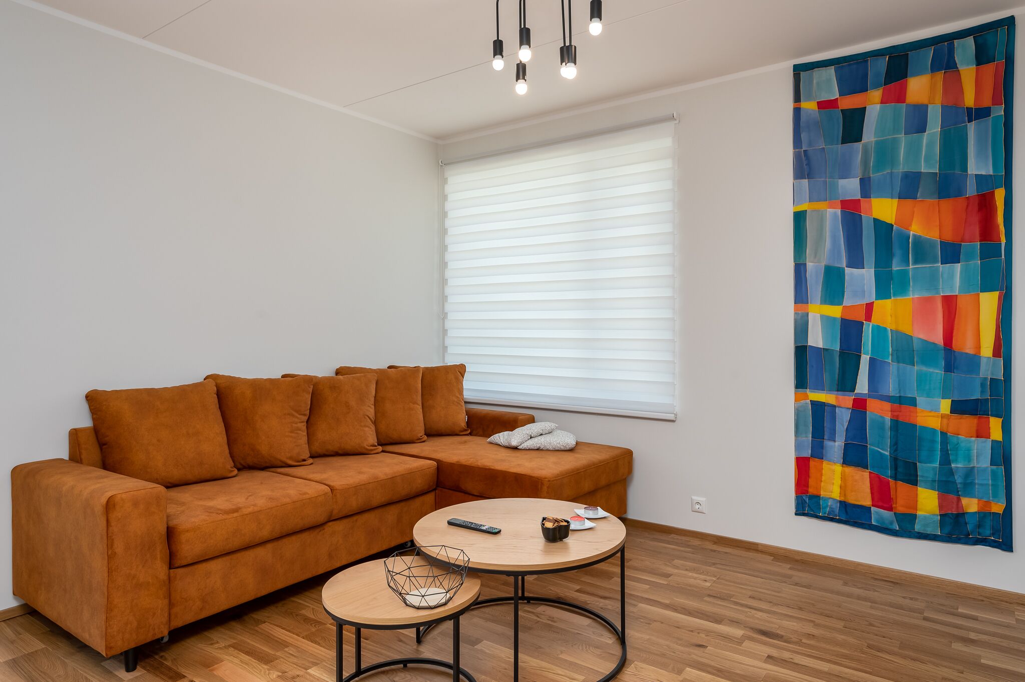 Un salon avec un canapé marron, une table basse ronde et un tableau abstrait aux couleurs vives accroché au mur.