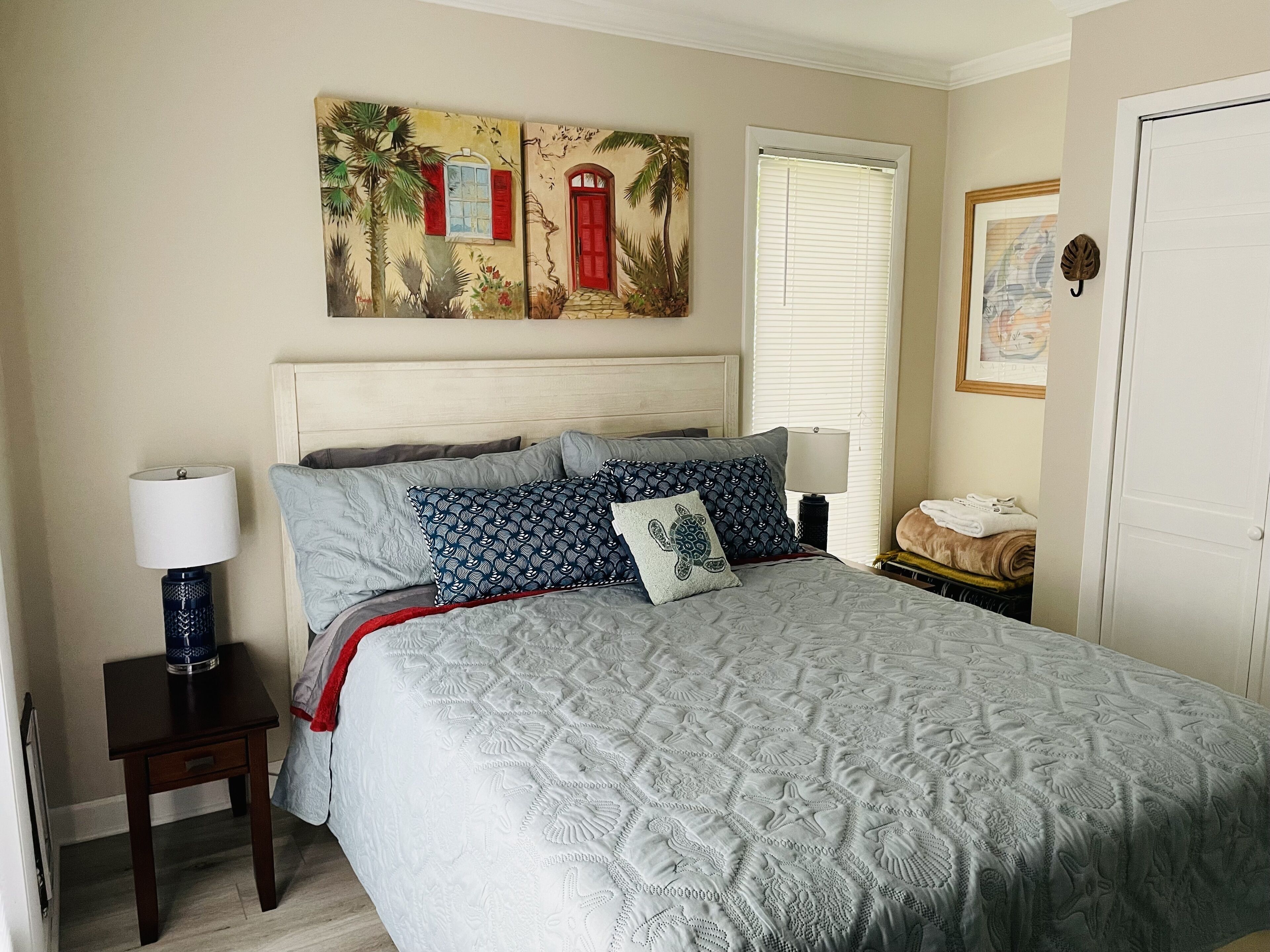 A neatly arranged bedroom with a bed, bedside tables, a painting, and a door.