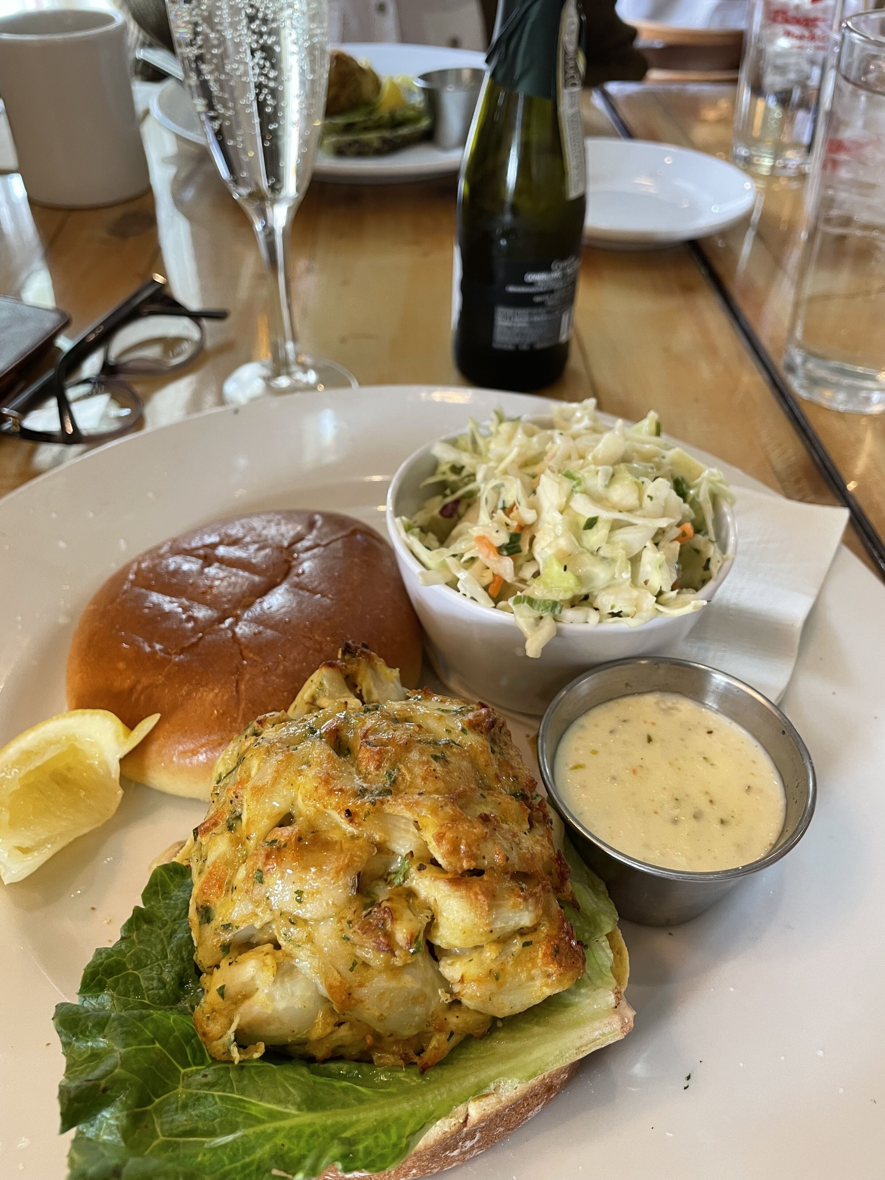 Un repas composé d’un sandwich au poulet, d’une salade de chou et d’une petite portion de sauce, le tout servi sur une assiette.