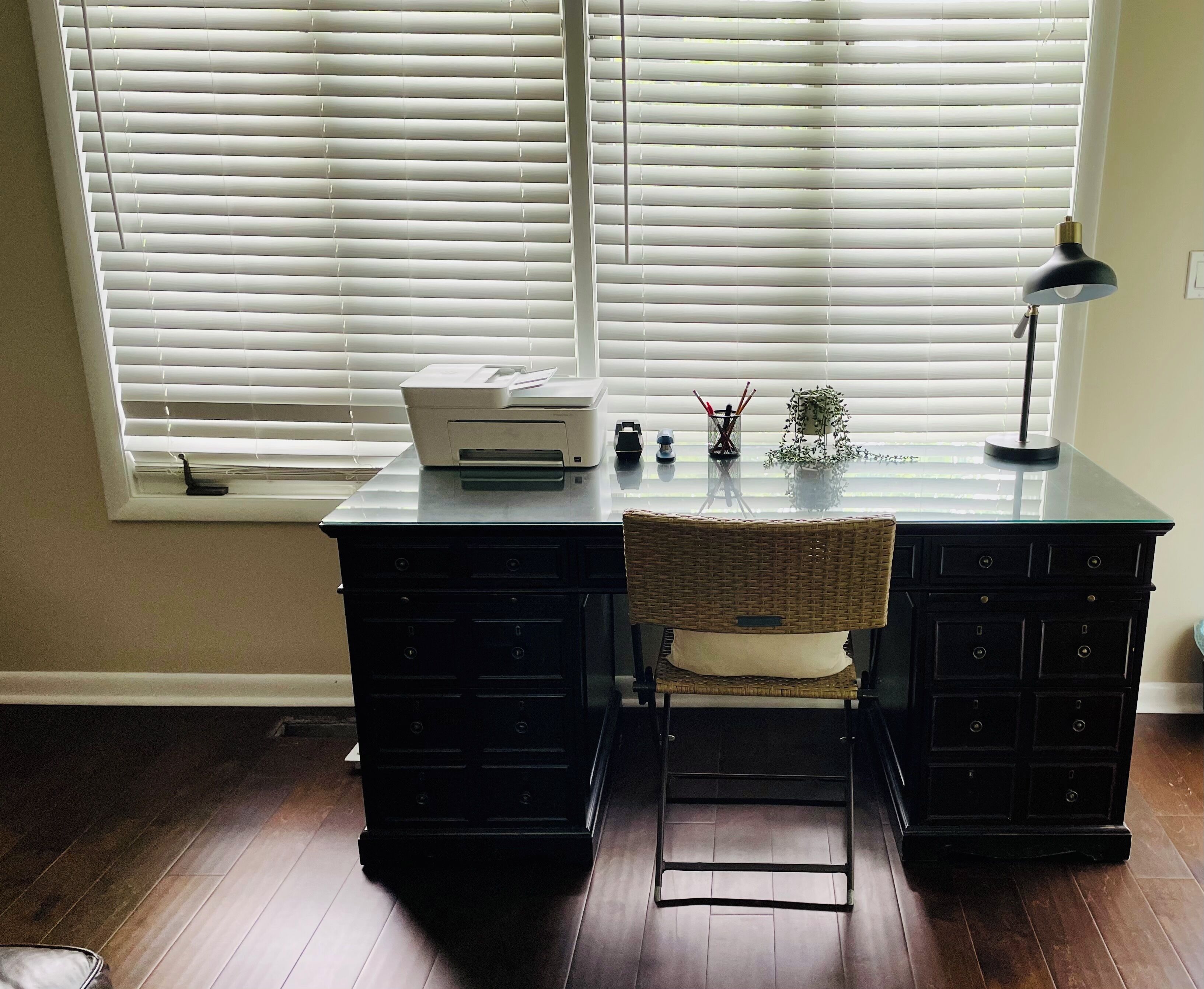 A workspace with a desk, chair, printer, lamp, and window blinds.