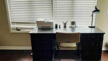 A workspace with a desk, chair, printer, lamp, and window blinds.
