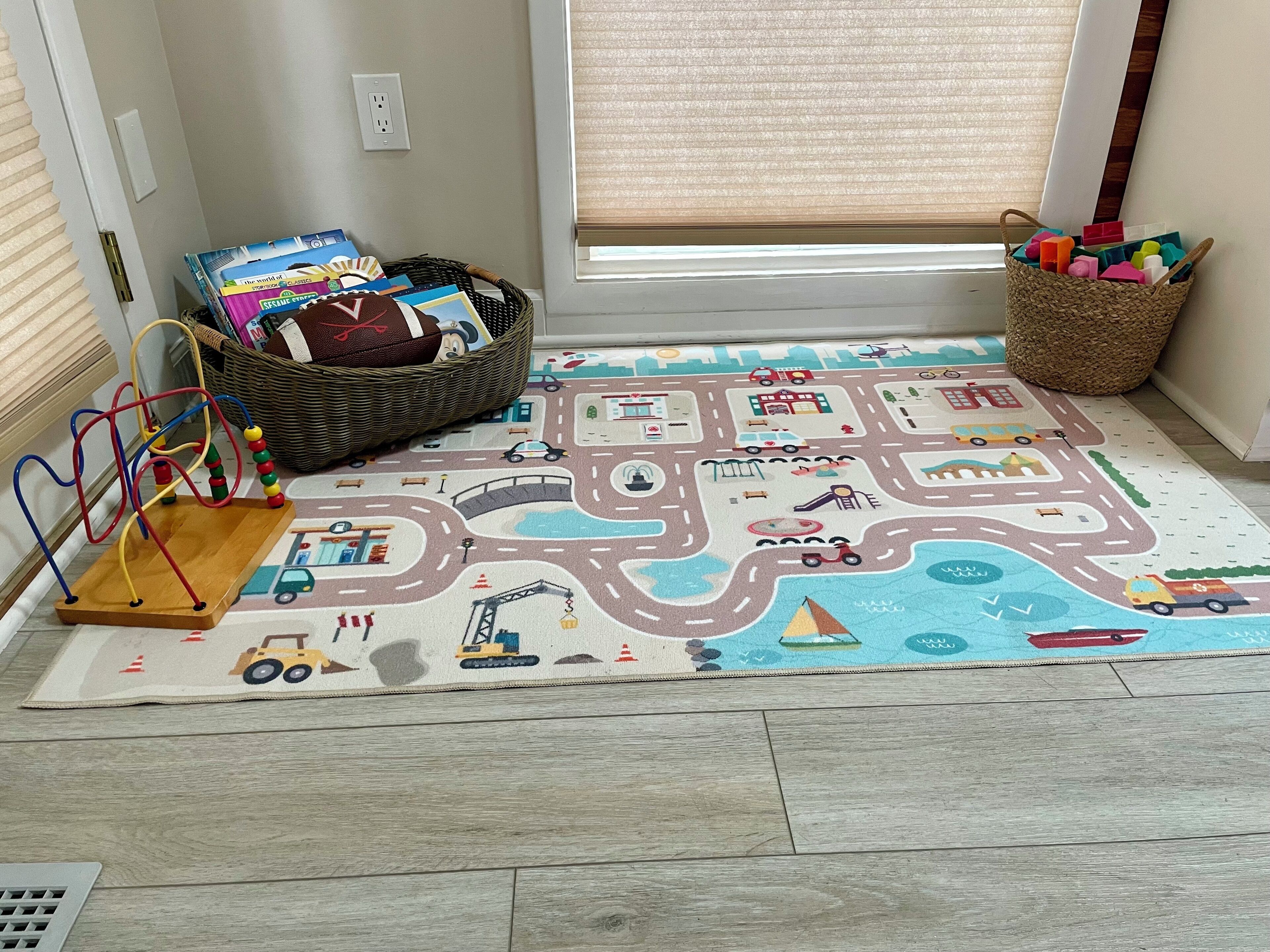 Un espace de jeux avec un tapis représentant une carte routière, un ensemble de trains miniatures et un panier rempli de jouets.