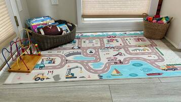 Un espace de jeux avec un tapis représentant une carte routière, un ensemble de trains miniatures et un panier rempli de jouets.