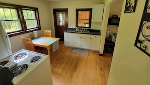 A kitchen with wooden cabinets, a stove, a dining table with chairs, and a window with a view of greenery. - Cabin on 25 Acres of Forest (Bessemer)