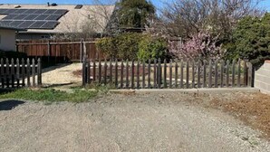 A residential property with a fenced yard, solar panels on the roof, and a variety of trees and shrubs. - Full Kitchen Studio w/ AC (Castro Valley)