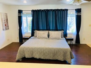 Une chambre à coucher avec un grand lit, des rideaux foncés et une fenêtre donnant sur des arbres.