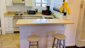 A modern kitchen with white cabinets, a central island with stools, a stove, and a sink. - Full Kitchen Studio w/ AC (Castro Valley)
