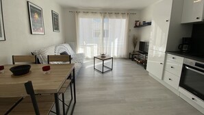 Une cuisine moderne avec des meubles blancs, une table à manger avec des chaises, un téléviseur et une machine à café.