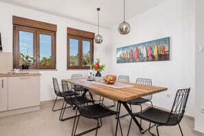 A dining area with a wooden table, black wire chairs, and a painting of sailboats on the wall.