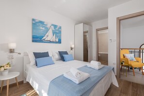 A modern hotel room with a large bed, a painting of sailboats, a balcony with a yellow chair, and a wooden floor.