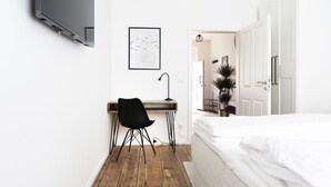 Una camera da letto con pavimento in legno, un letto, una scrivania con sedia e un televisore montato a parete.