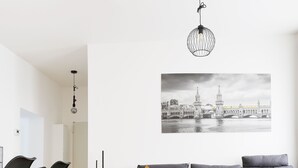 Un soggiorno moderno con pavimento in legno, un divano grigio, sedie nere e una lampada a sospensione.