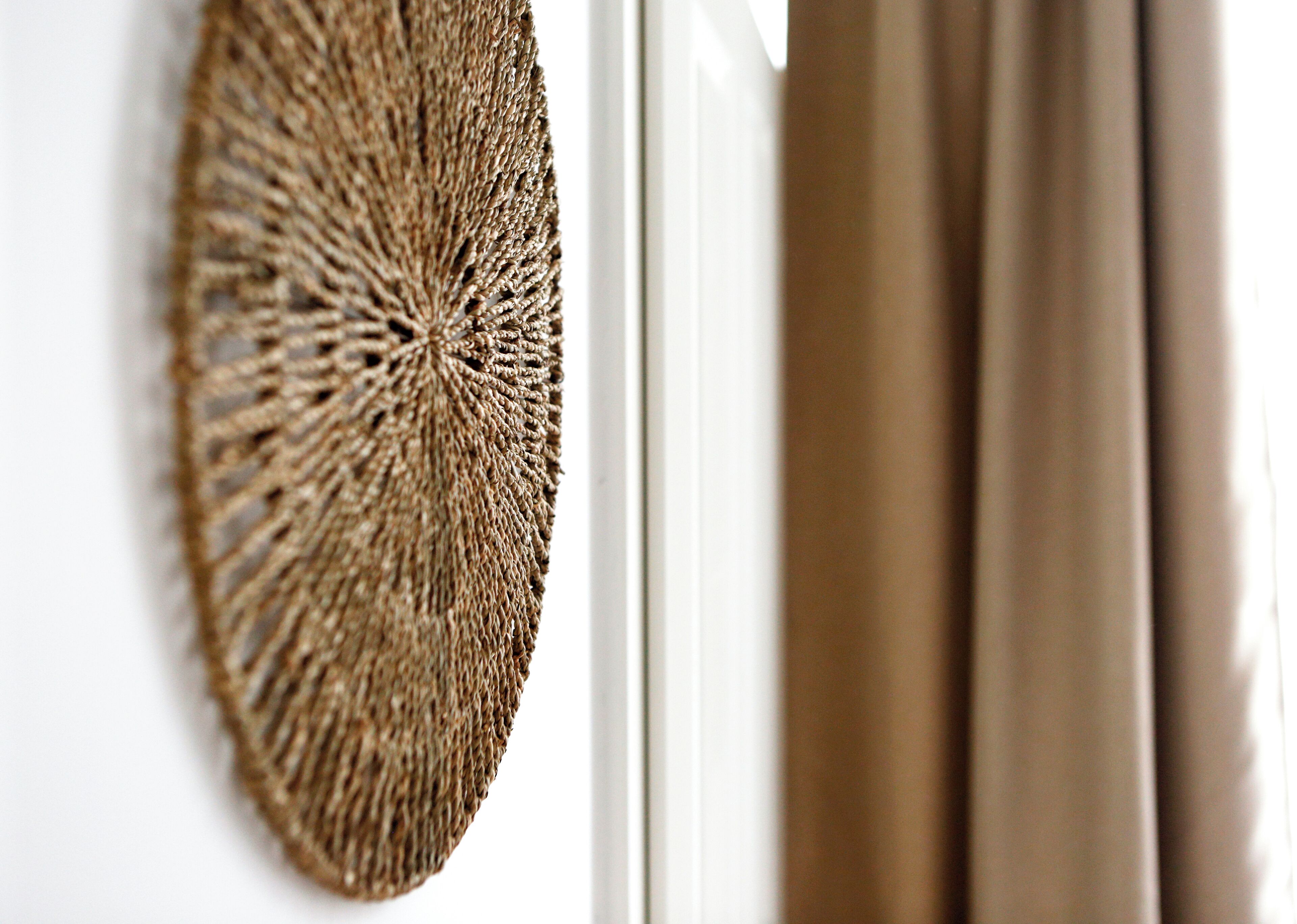 A close-up of a textured wall hanging and a window with curtains.