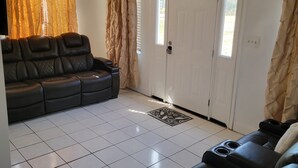 Un soggiorno con un divano in pelle nera, una ventola a soffitto e una porta bianca.