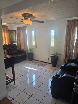 A living room with a ceiling fan, a black leather sofa, a coffee table, and a potted plant.