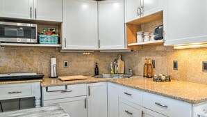 Een moderne keuken met witte kasten, granieten werkbladen, een magnetron, een broodrooster en een koffiezetapparaat.