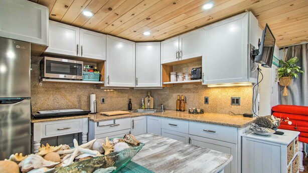 Een moderne keuken met witte kasten, een roestvrijstalen koelkast, een magnetron en een spoelbak. Er is een aanrecht met diverse keukengerei en een schaal met zeevruchten op het eiland.
