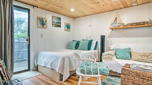 Een knus slaapkamer met een houten plafond, een bed met wit en groen beddengoed, een witte stoel en een rieten bijzettafeltje.