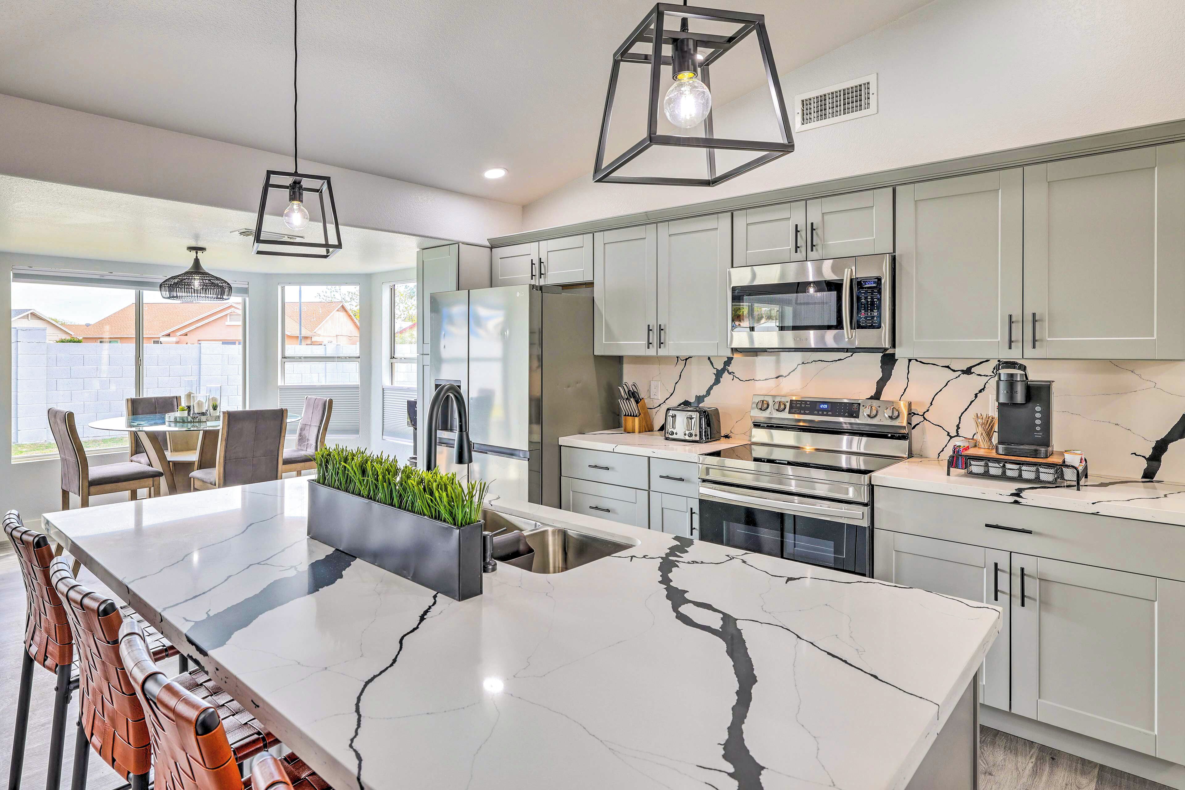 A modern kitchen with a marble island, stainless steel appliances, and light grey cabinets.