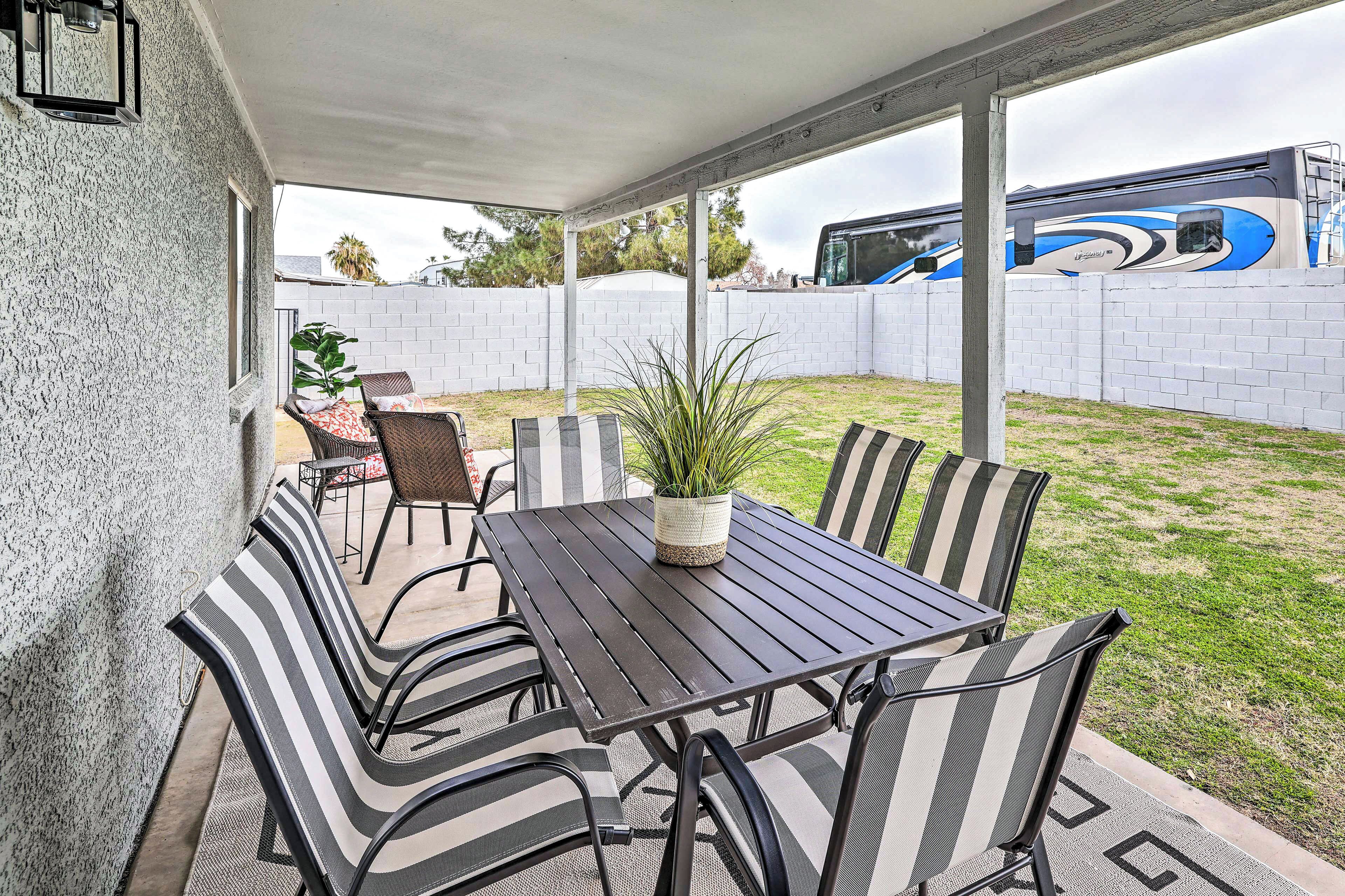 A covered patio with a table and chairs, a potted plant, and a view of a parked bus.
