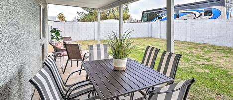 A covered patio with a table and chairs, a potted plant, and a view of a parked bus.
