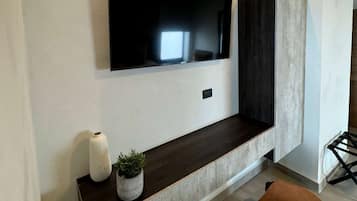 Una sala de estar moderna con un televisor de pantalla plana montado sobre una consola de madera oscura, un jarrón blanco con una planta y un sillón marrón.