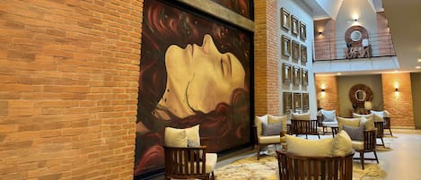 Un vestíbulo con paredes de ladrillo, un mural abstracto de gran tamaño y una zona de estar con sillas acolchadas.