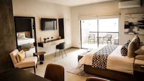 A modern hotel room with a large bed, a sofa, a TV, a balcony with chairs, and a sliding glass door. - Esplendor by Wyndham San Luis Potosi (San Luis Potosi)