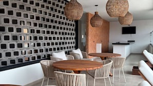 A modern lounge area with wicker furniture, a concrete wall with square cutouts, and a flat-screen TV mounted on the wall. - Esplendor by Wyndham San Luis Potosi (San Luis Potosi)