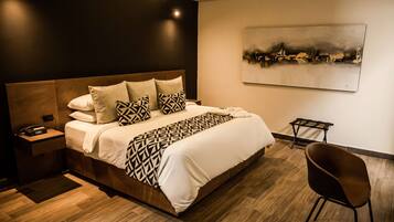 Una habitación de hotel moderna con una cama grande, una mesita de noche con teléfono, una silla y un cuadro en la pared.