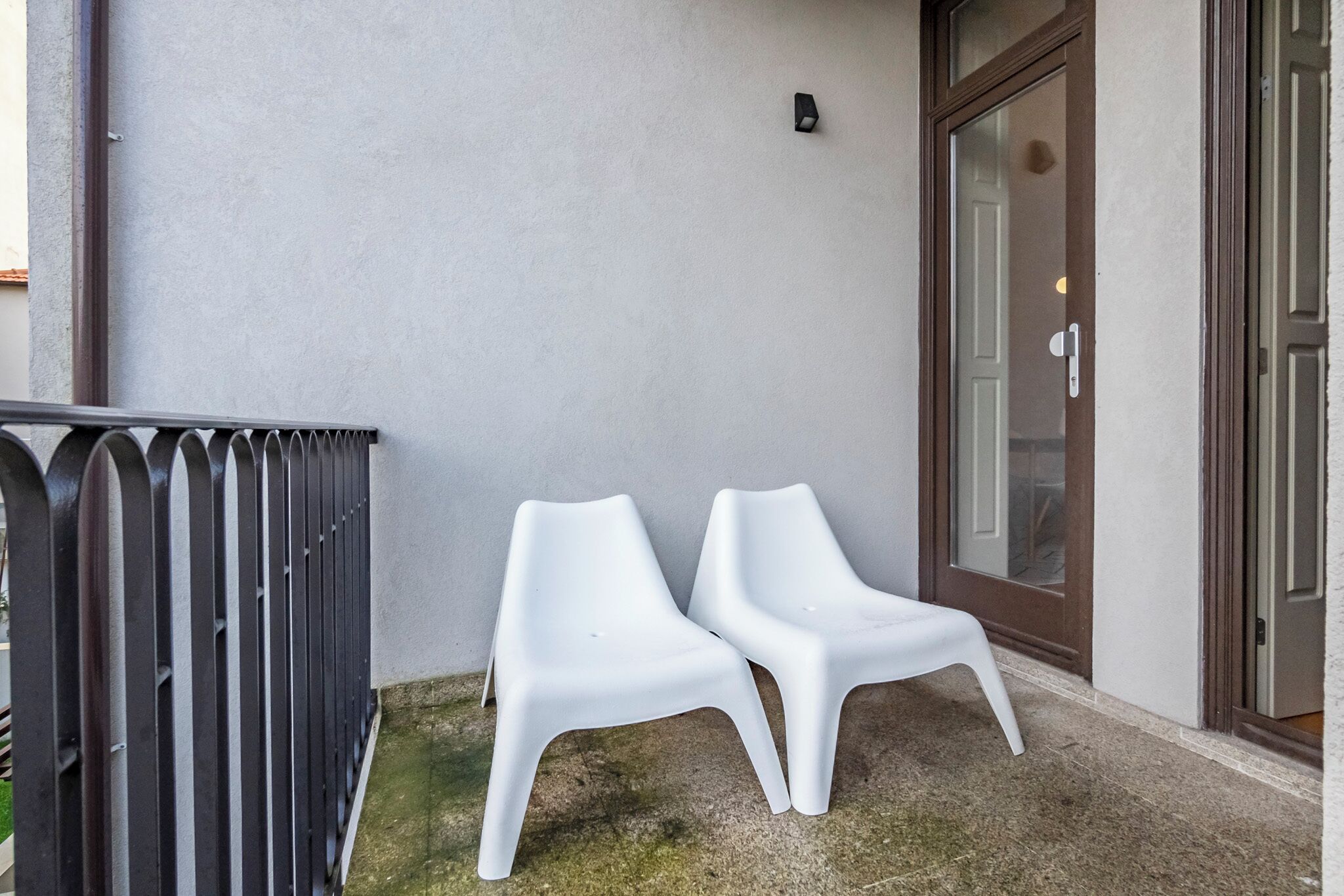 Two white plastic chairs outside a building with a metal fence and a glass door.