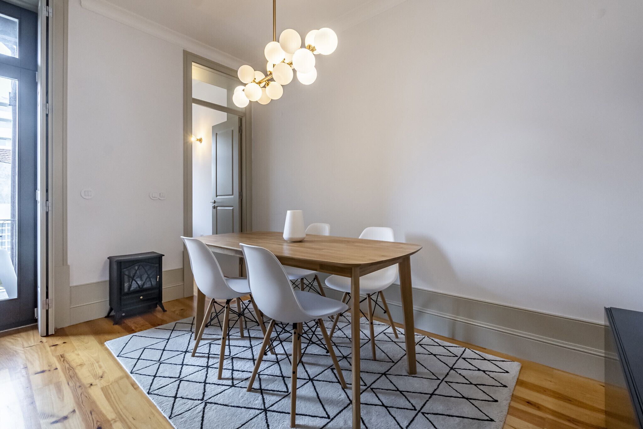 A dining area with a wooden table, white chairs, and a geometric patterned rug.
