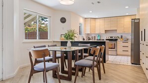 A modern kitchen with wooden cabinets, a central island, and a dining area with a glass table and chairs. - Your home away from home! (Round Rock)